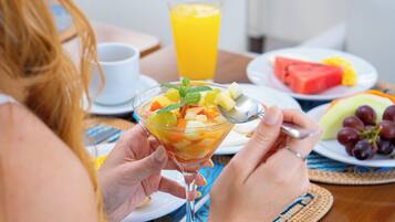 Una persona sosteniendo una ensalada de frutas en un vaso, un vaso de jugo de naranja y platos con sandía y uvas.