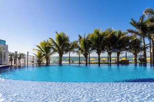 Piscina cristallina blu circondata da palme e ombrelloni, con vista sull'oceano.