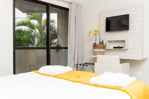 Camera d'albergo con un letto, una TV a muro, una piccola scrivania con una sedia e una finestra vista palme.