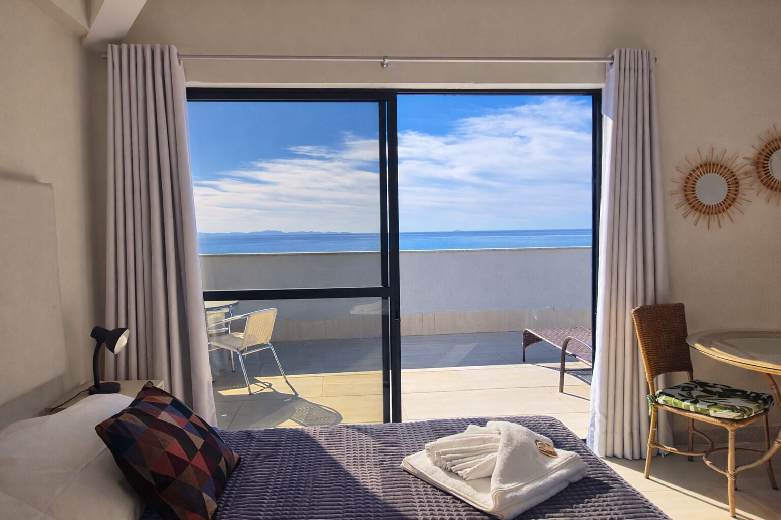 Habitación de hotel con cama, una mesita, una silla y vistas al mar a través de una puerta corrediza.