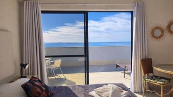 Habitación de hotel con cama, una mesita, una silla y vistas al mar a través de una puerta corrediza.