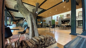 A spacious indoor area with a large tree trunk centerpiece, wooden flooring, and a stack of firewood.