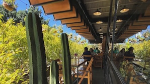 An outdoor dining area with wooden tables and chairs, surrounded by cacti and greenery.