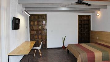 Una habitación con un escritorio de madera, una silla, una cama con ropa de cama a rayas, una planta en maceta y un ventilador de techo.
