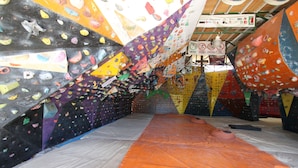 An indoor climbing gym with various climbing walls and a padded floor.