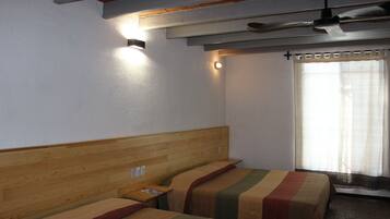 Habitación de hotel con dos camas, cabeceros de madera, ventilador de techo y ventana con cortinas.