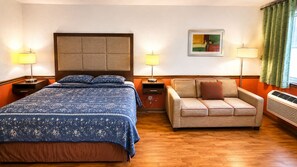 Une chambre d’hôtel comprenant un lit, un canapé, deux tables de chevet avec des lampes, une œuvre d’art accrochée au mur et une fenêtre avec des rideaux.