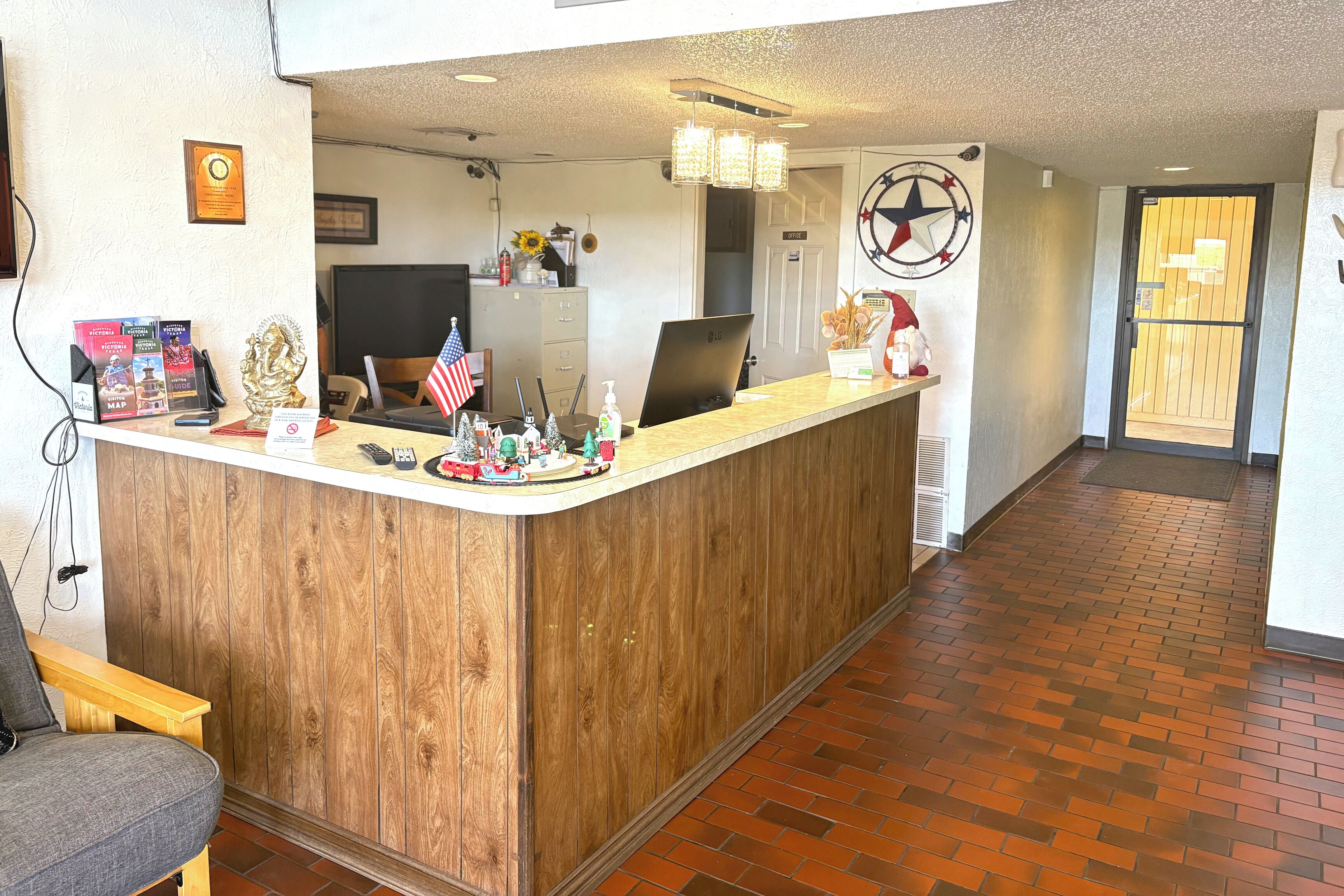 A reception area with a wooden counter, a desk, and a chair. There are various items on the counter, including a small American flag, a bottle of hand sanitizer, and a decorative statue.
