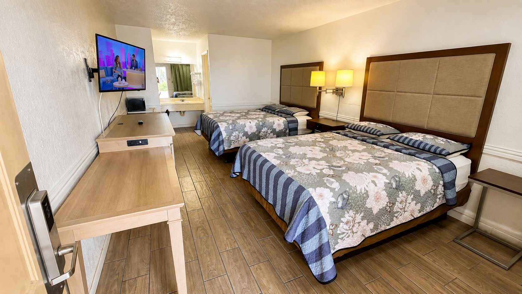 A hotel room with two beds, a desk, a television, and a mirror.