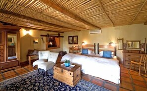 A rustic bedroom with a wooden ceiling, two beds, a wooden chest, and a patterned rug. - De Opstal (Oudtshoorn)