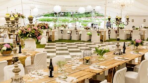 A tented outdoor event space with checkered flooring, round tables set with white tablecloths, and chandeliers. - De Opstal (Oudtshoorn)