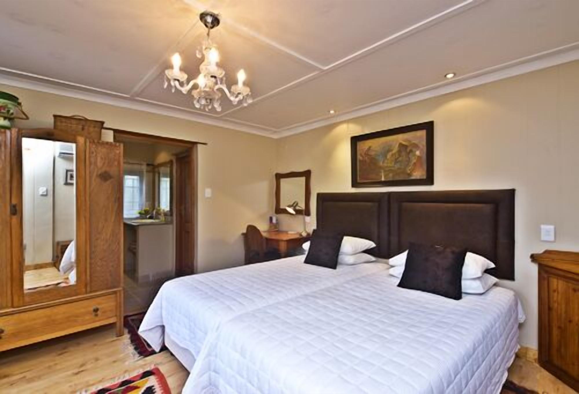 Une chambre à coucher avec un grand lit, une armoire en bois, un miroir et un lustre.