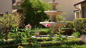A tiered stone fountain surrounded by lush greenery and flowering plants in a courtyard. - Budmarsh Country Lodge (Magaliesberg)