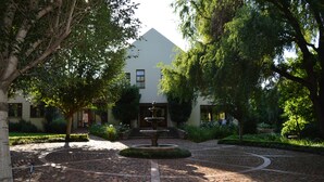 A courtyard with a fountain, paved walkway, and a building with a triangular roof. - Budmarsh Country Lodge (Magaliesberg)