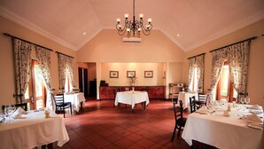 A dining area with multiple tables set for dining, a chandelier, and a red-tiled floor. - Budmarsh Country Lodge (Magaliesberg)