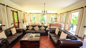 A spacious living room with leather sofas, a wooden coffee table, and a chandelier. - Budmarsh Country Lodge (Magaliesberg)