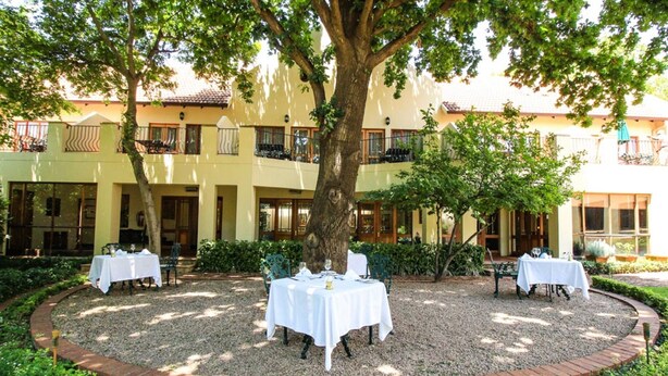 A courtyard with tables set for dining, surrounded by a brick border and greenery, with a building in the background. - Budmarsh Country Lodge (Magaliesberg)