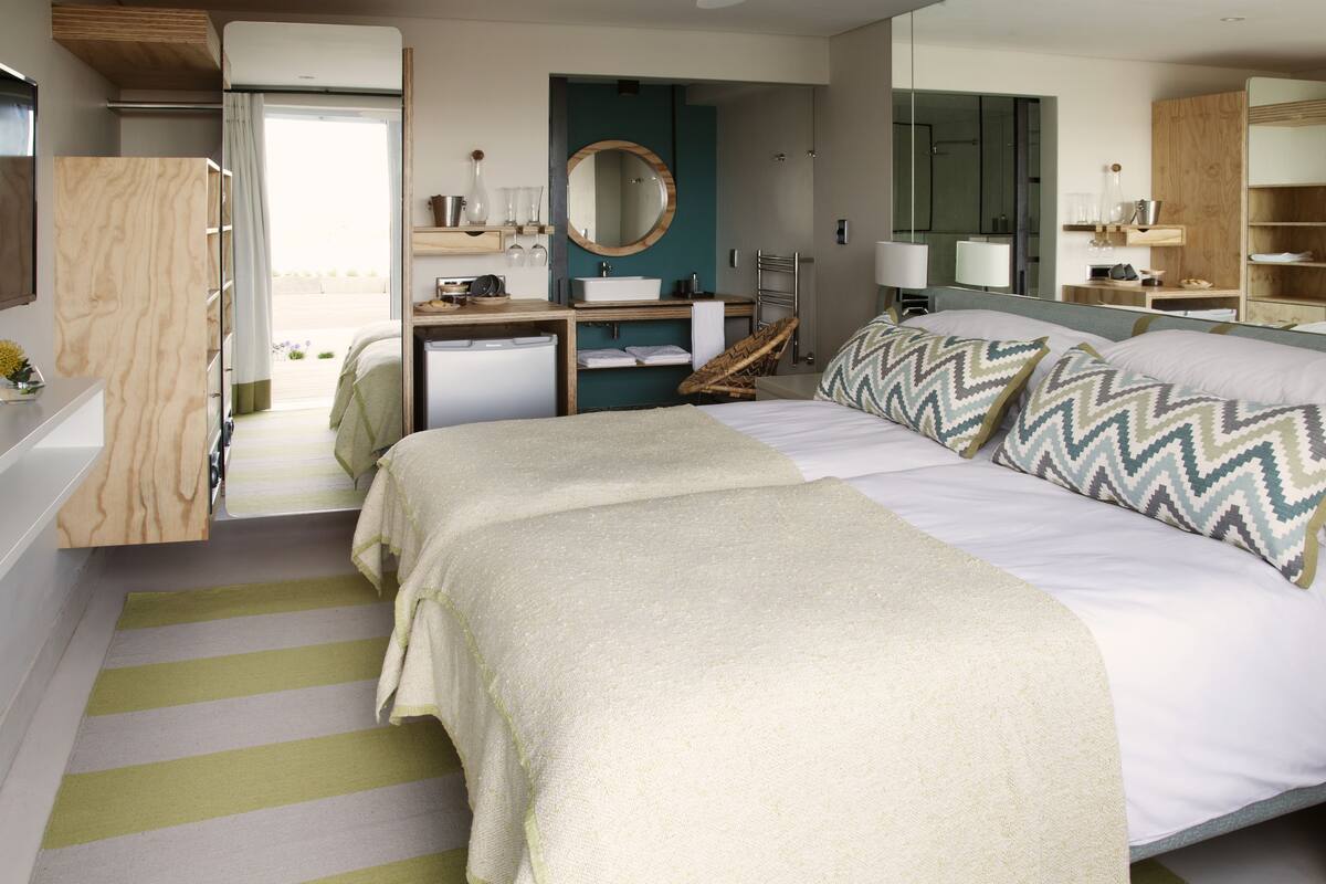 Habitación de hotel con cama, mesitas de noche, espejo, lavamanos y vistas al exterior.