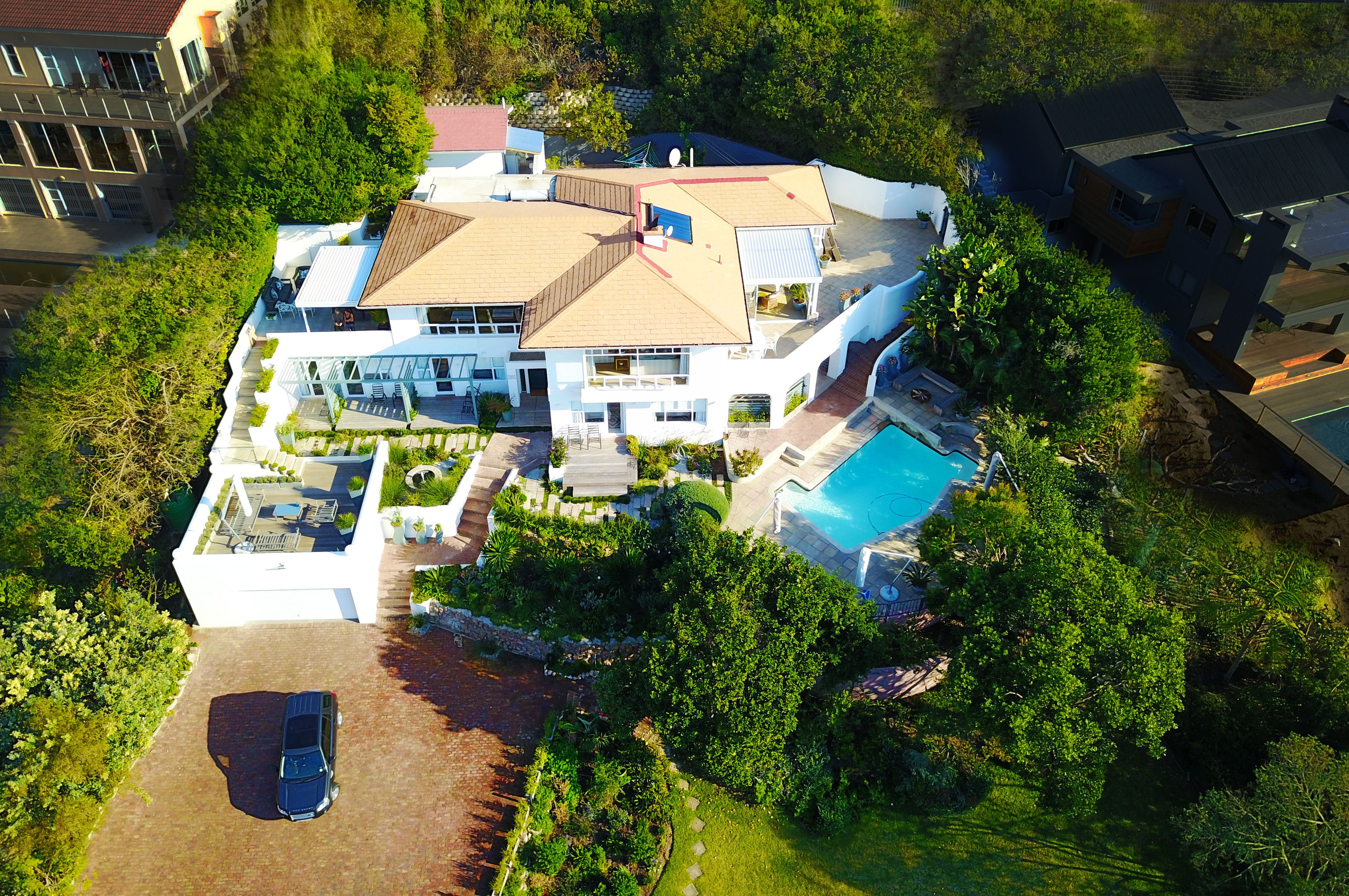 A large, modern house with a swimming pool, surrounded by lush greenery.
