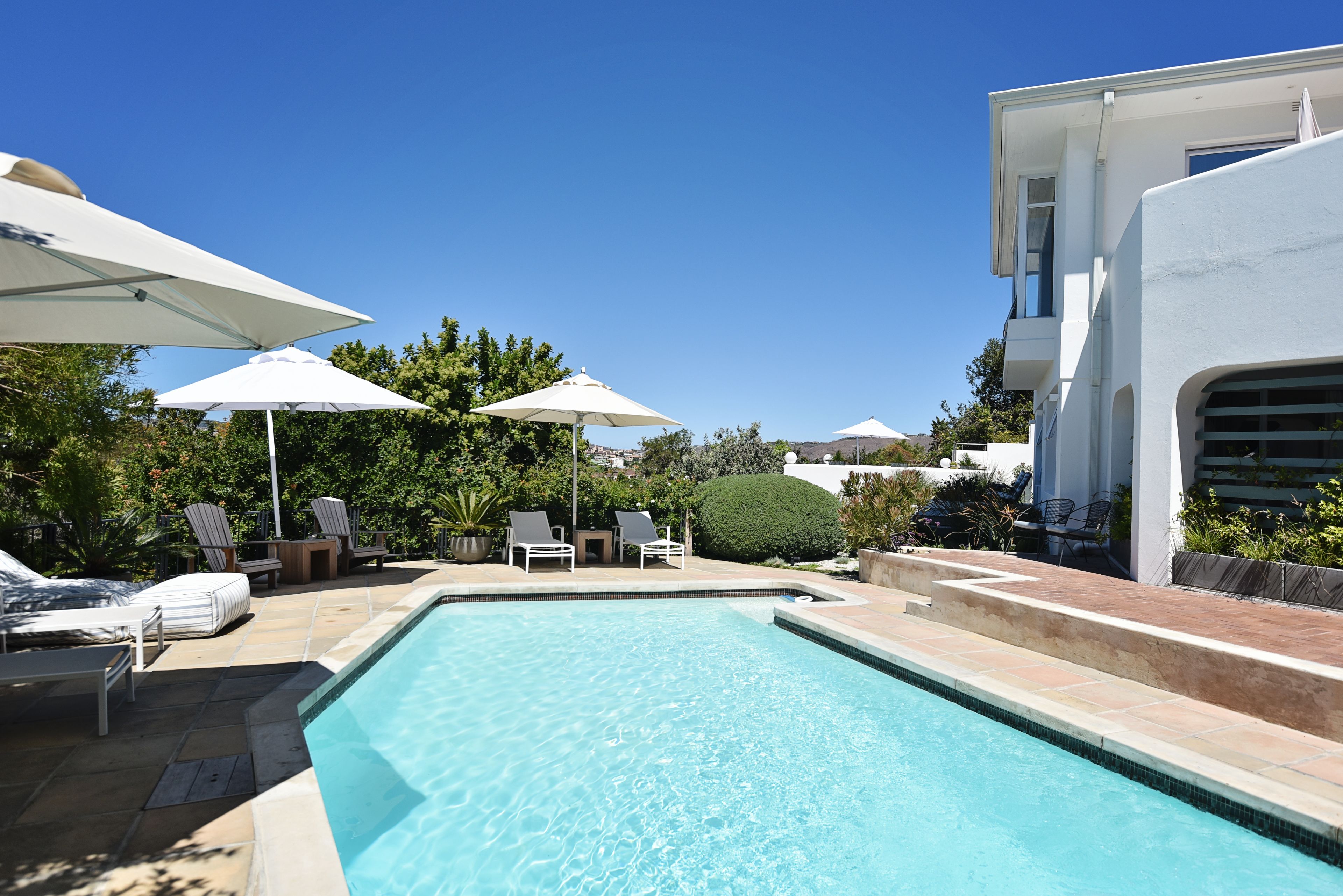Piscina com espreguiçadeiras e guarda-sóis, cercada por vegetação e um edifício moderno.