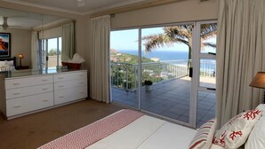 Un dormitorio con una cama grande, un aparador, un espejo y un balcón con vistas al mar.