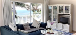 A living room with a sofa, a coffee table, and a TV. There is a balcony with a view of the ocean. - Acacia Crescent Seaview Manor (Westbrook)