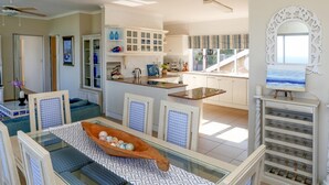 Amplia sala de estar con una mesa de comedor, una cocina con armarios blancos y vista al océano.