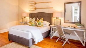 Quarto com cama, abajures, escrivaninha, cadeira, espelho e luminária de teto diferenciada.