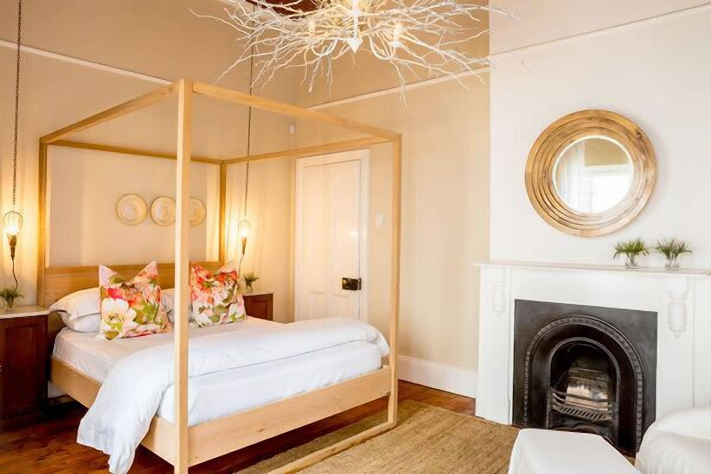 A four-poster bed with a white canopy, a fireplace, and a round mirror on the wall.