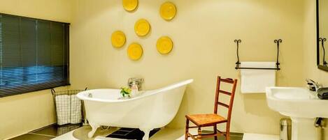 A bathroom with a freestanding bathtub, a wooden chair, a sink, and a mirror.