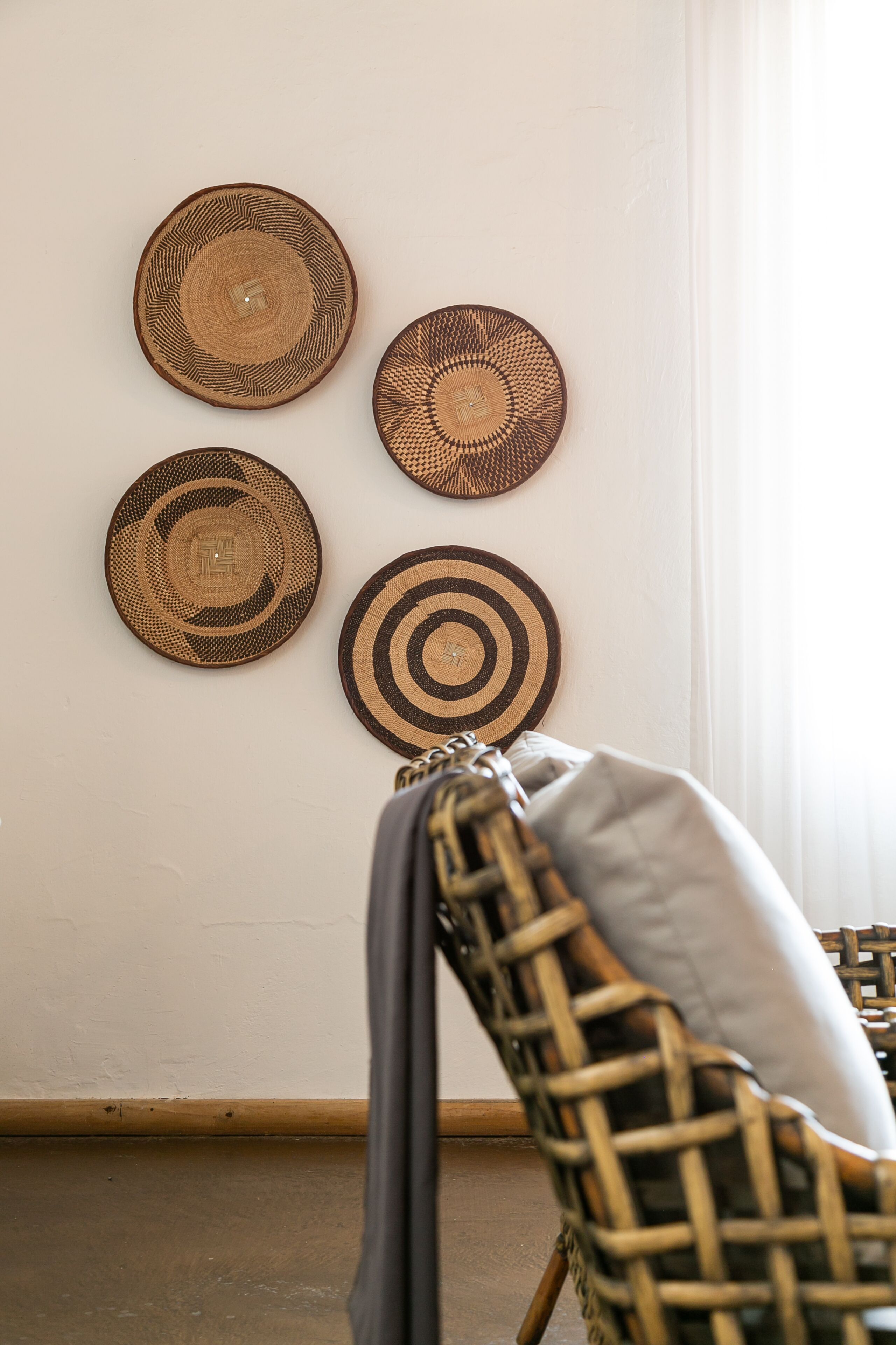 A room with a woven chair and a wall adorned with four circular woven wall hangings.