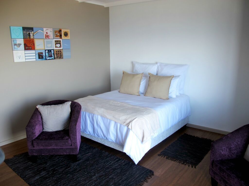 Un dormitorio con cama, dos sillas, una obra de arte en la pared y una alfombra oscura.