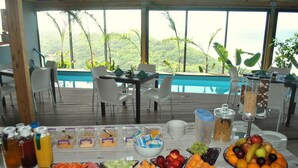 A buffet table with various fruits, vegetables, and beverages, set against a backdrop of a pool and lush greenery. - Wilderness Beach Resort (Wilderness)