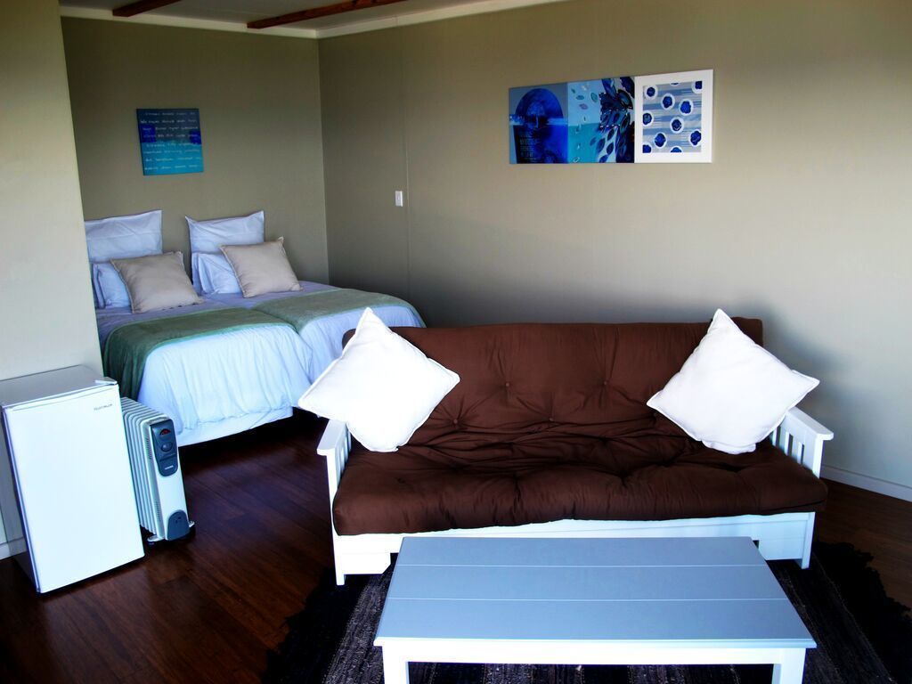 Una habitación con una cama, un sofá marrón, una mesa blanca y un radiador.