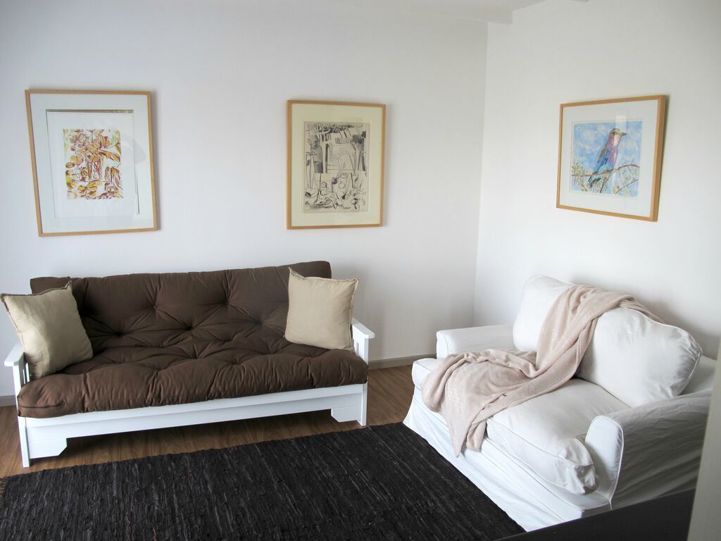 A living room with a brown sofa and a white sofa against a white wall, with three framed artworks above them.