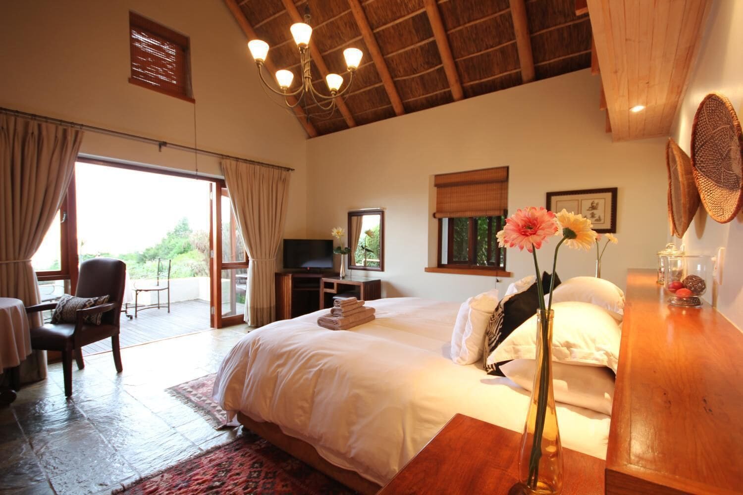 A spacious bedroom with a large bed, a desk, a TV, and a balcony with a chair.