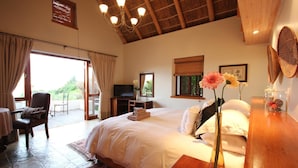 A spacious bedroom with a large bed, a desk, a TV, and a balcony with a chair. - Paradise Cove Country House (Wilderness)