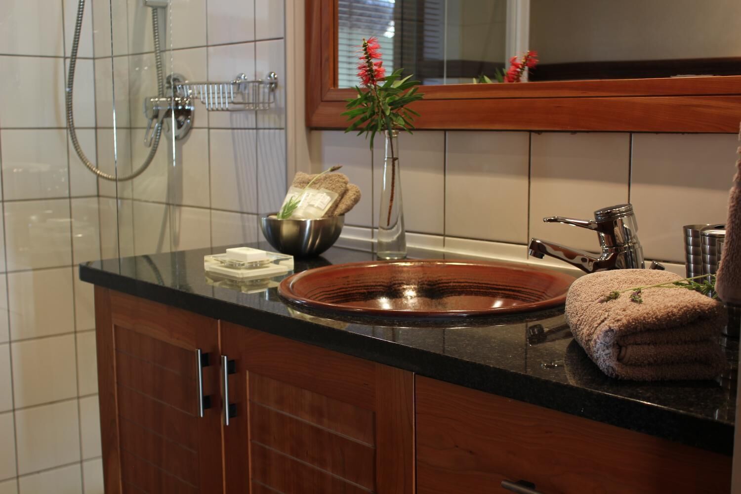 A bathroom with a wooden vanity, a copper sink, a glass shower enclosure, and a mirror above the sink.
