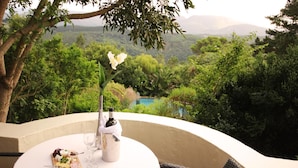 A table set with a bottle of champagne, glasses, and a cheese board, overlooking a lush landscape with a pool. - Paradise Cove Country House (Wilderness)