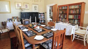 A dining room with a wooden table set for six, surrounded by chairs. A bookshelf filled with books is visible in the background. - Villa Bianca (Cape Town)