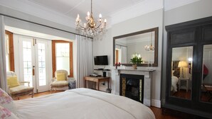A bedroom with a large bed, a television, a fireplace, and a mirror. - Villa Bianca (Cape Town)