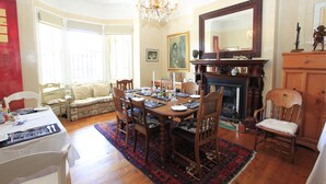 A dining room with a wooden table set for four, surrounded by chairs. There is a fireplace with a mantle, a large mirror above it, and a chandelier hanging from the ceiling. - Villa Bianca (Cape Town)