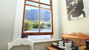 A room with a large window, a white chair, a wooden table with cups and a tray, and a wall-mounted picture. - Villa Bianca (Cape Town)