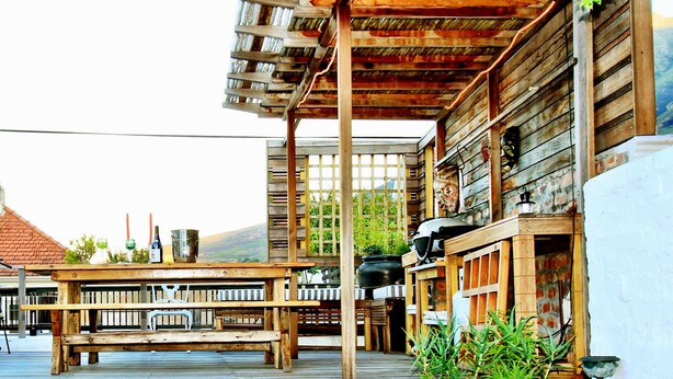 A wooden deck with a rustic outdoor seating area, including a table and chairs, and a planter with plants. - Villa Bianca (Cape Town)