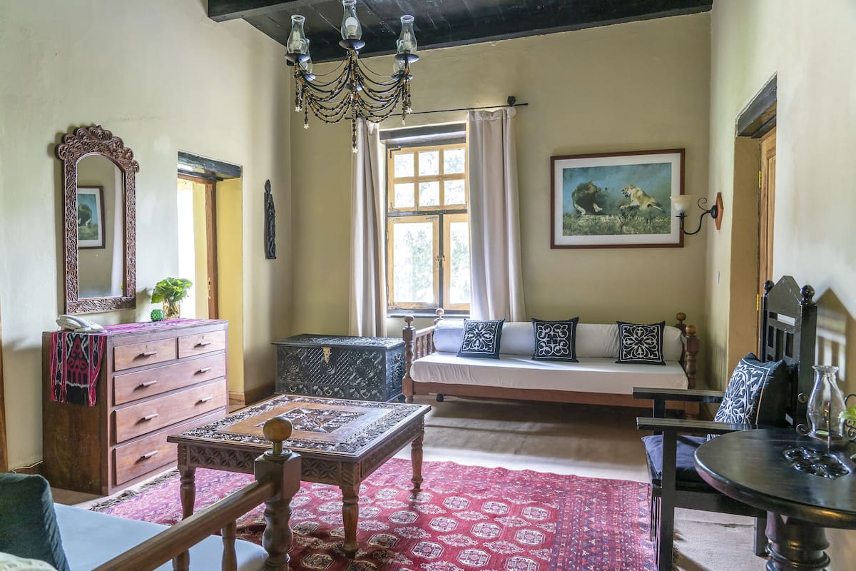 Una habitación tradicional con cama, una mesa de madera, un aparador, una araña y una ventana con cortinas.