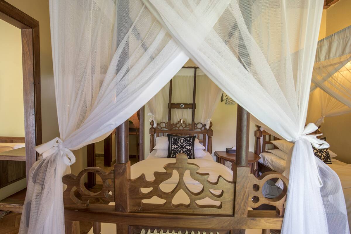 Una cama de madera con dosel, un espejo y una mesita de noche con lámpara.