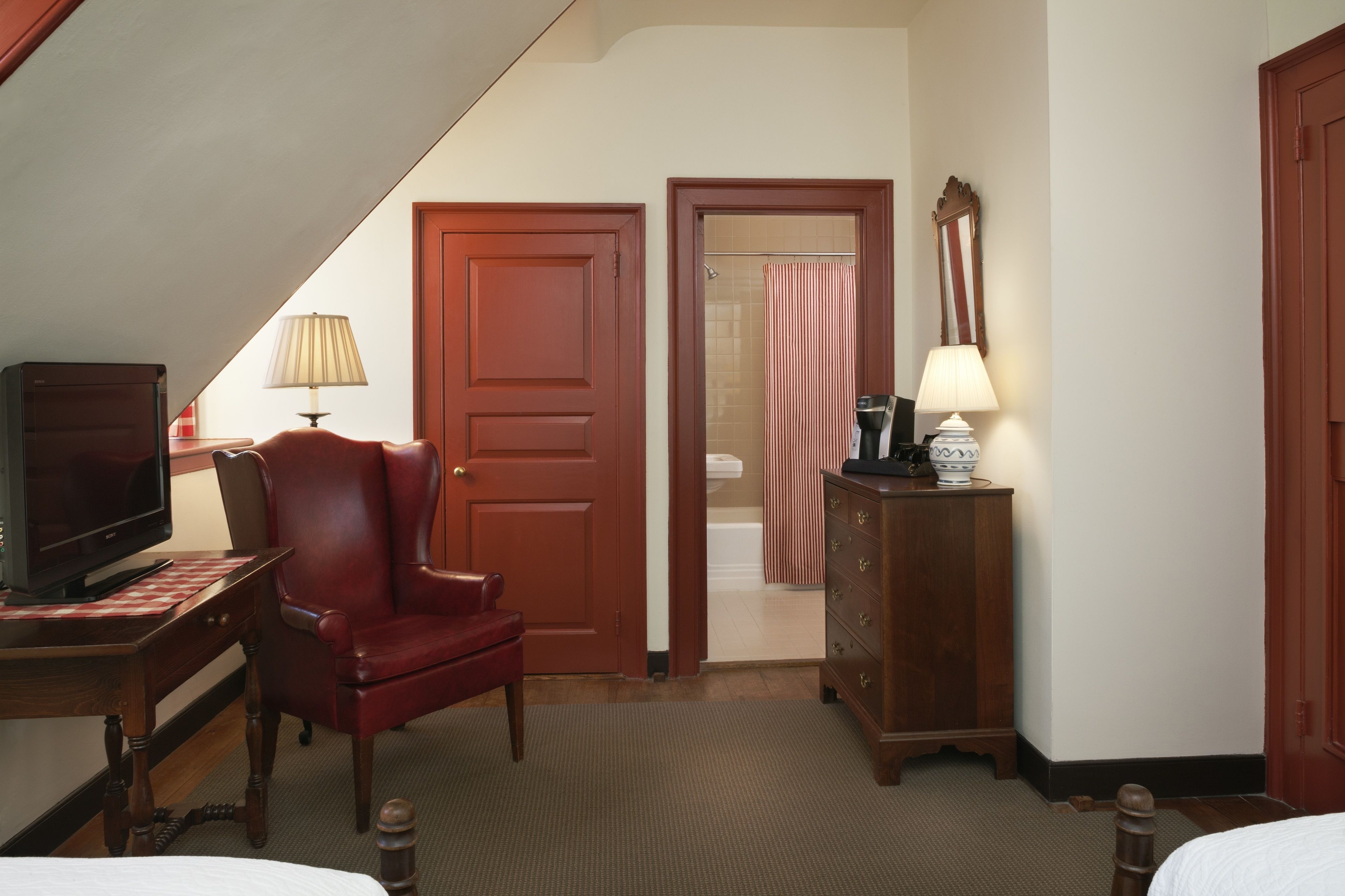 Habitación de hotel con escritorio, silla, televisor, cómoda y puerta que da a un baño.