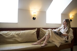 A person sitting on a sofa in a room with two wall-mounted lights and a window. - Colonial Houses, an Official Colonial Williamsburg Hotel (Williamsburg)