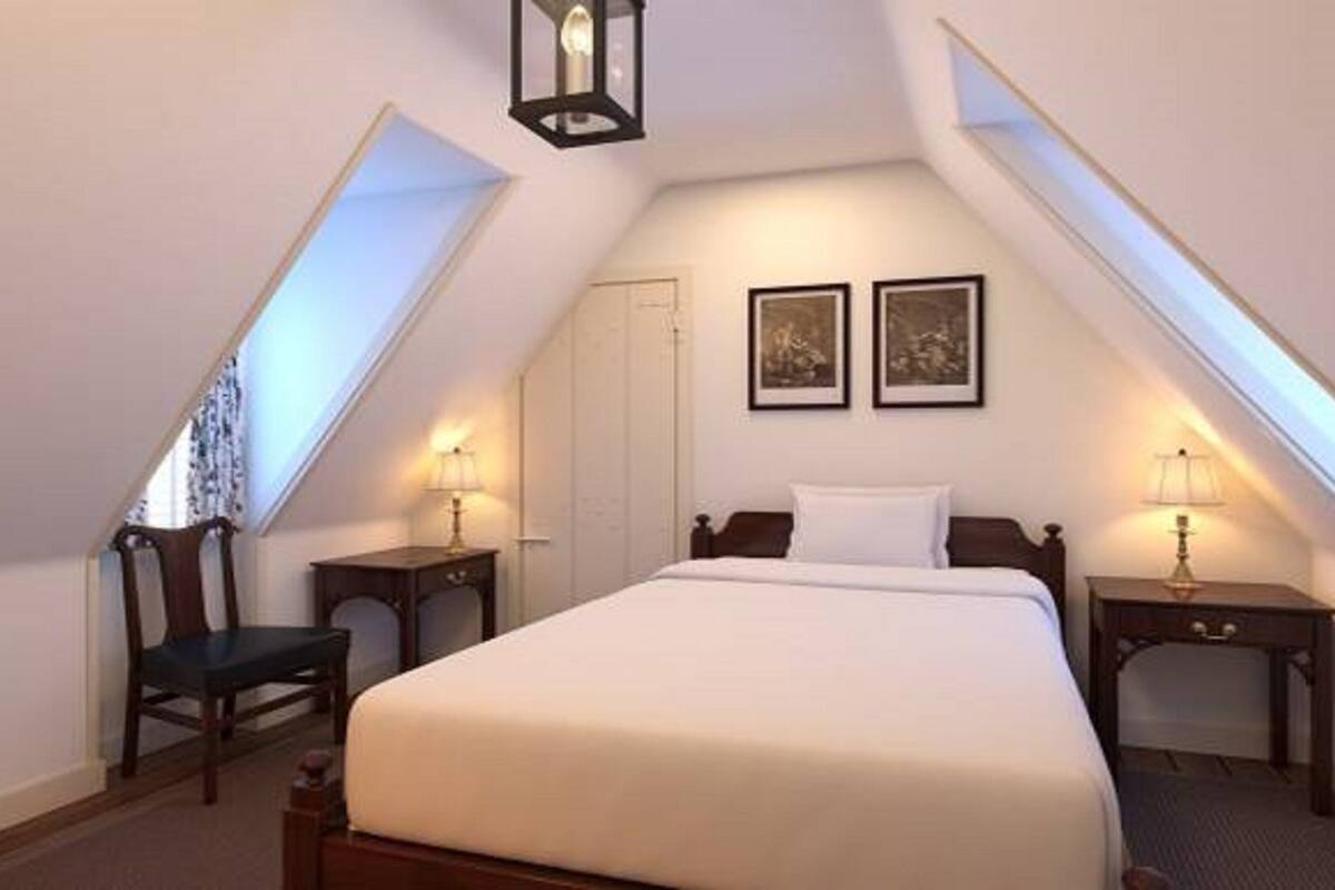 A bedroom with a large bed, two bedside tables, a chair, and two framed pictures on the wall.