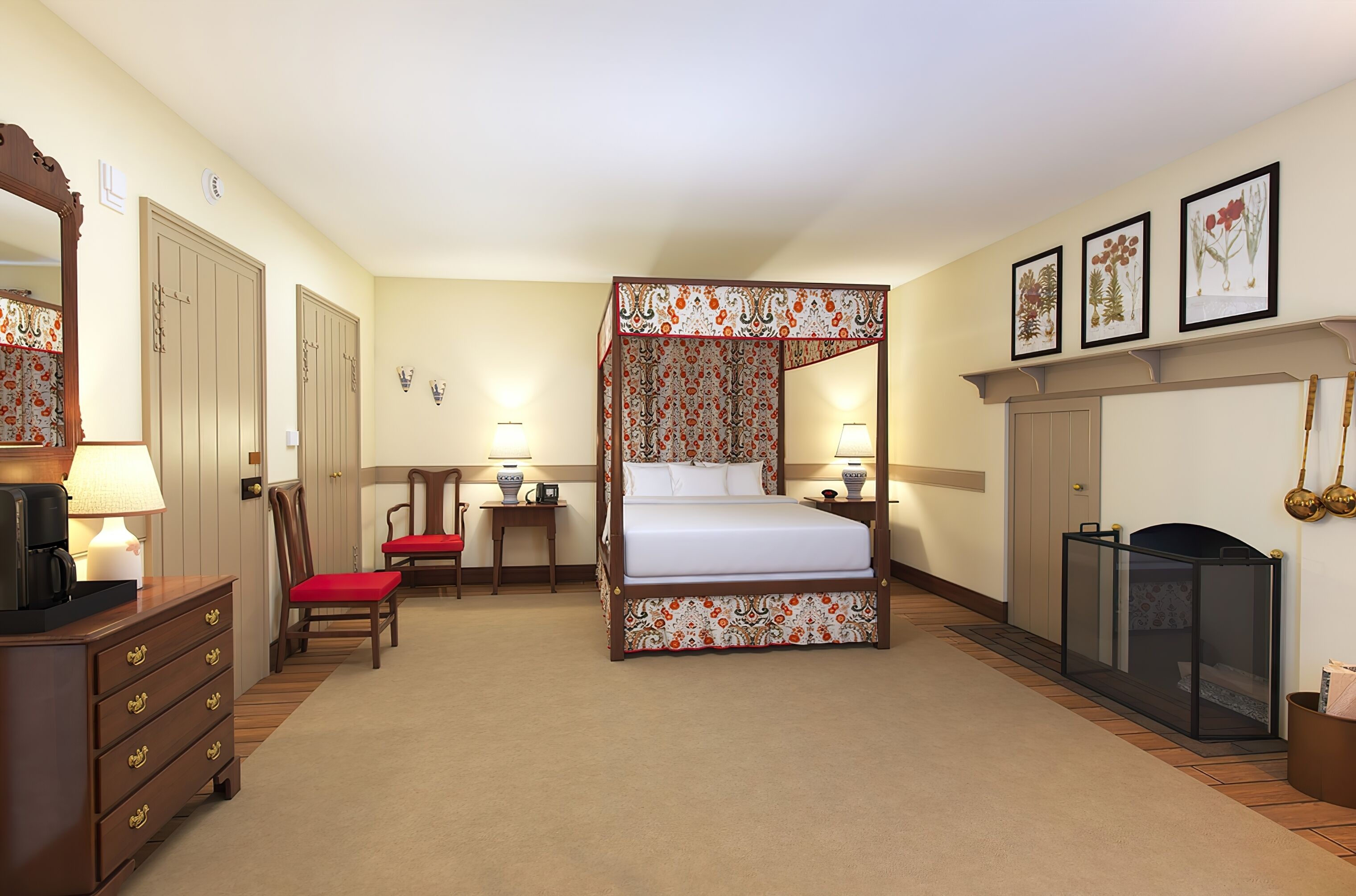 Een hemelbed met bloemenhemel, een houten dressoir met lades, een rode fauteuil, een tafeltje met een lamp en ingelijste botanische prints aan de muur.